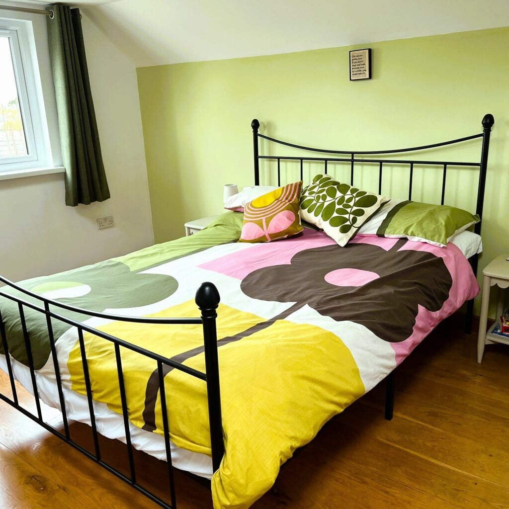 Bedroom with green wall behind bed, colourful Orla Kiely bedlinen